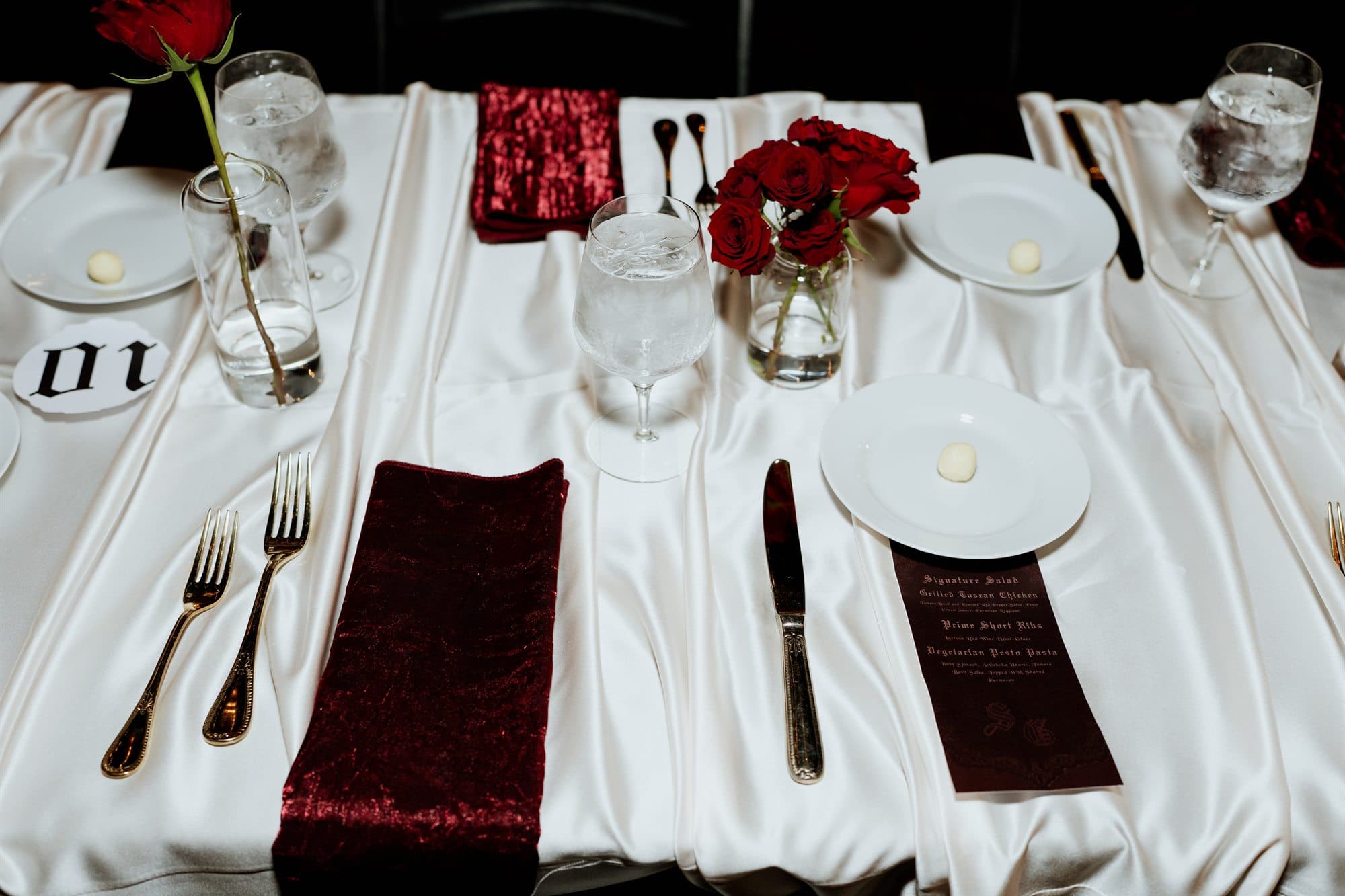 An ivory place setting with a burgundy velvet napkin, menu and red rose