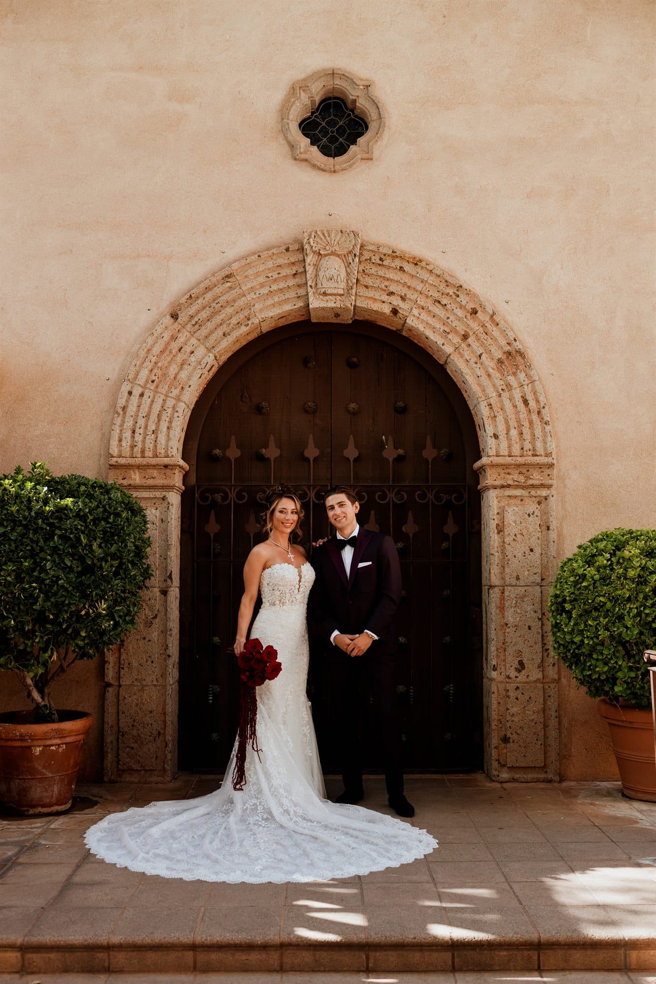 Sarah and Grant before a carved arched doorway at Tlaquepaque, her cathedral train spread across the stone
