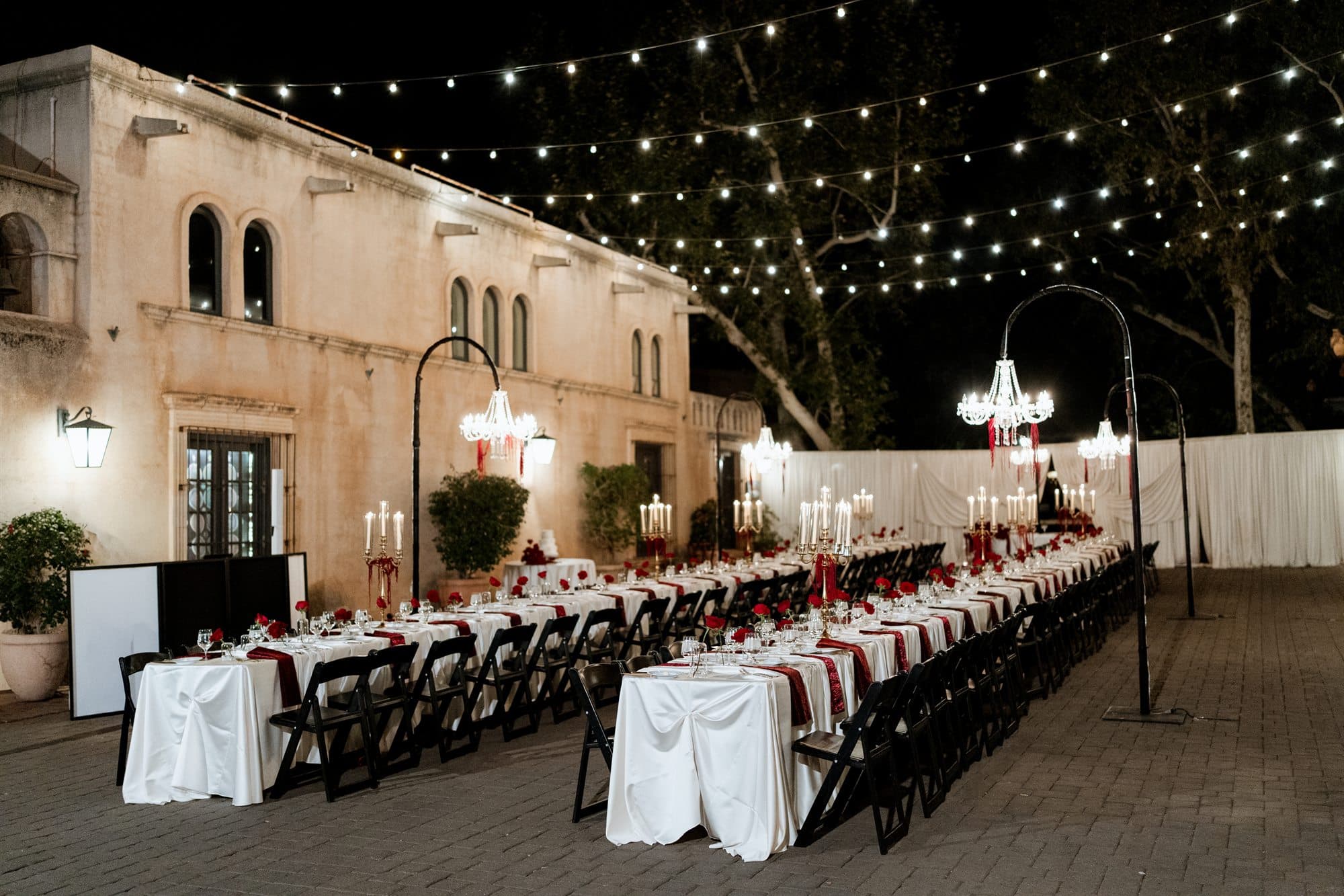 Rows of long banquet tables beneath string lights in the Tlaquepaque courtyard at dusk