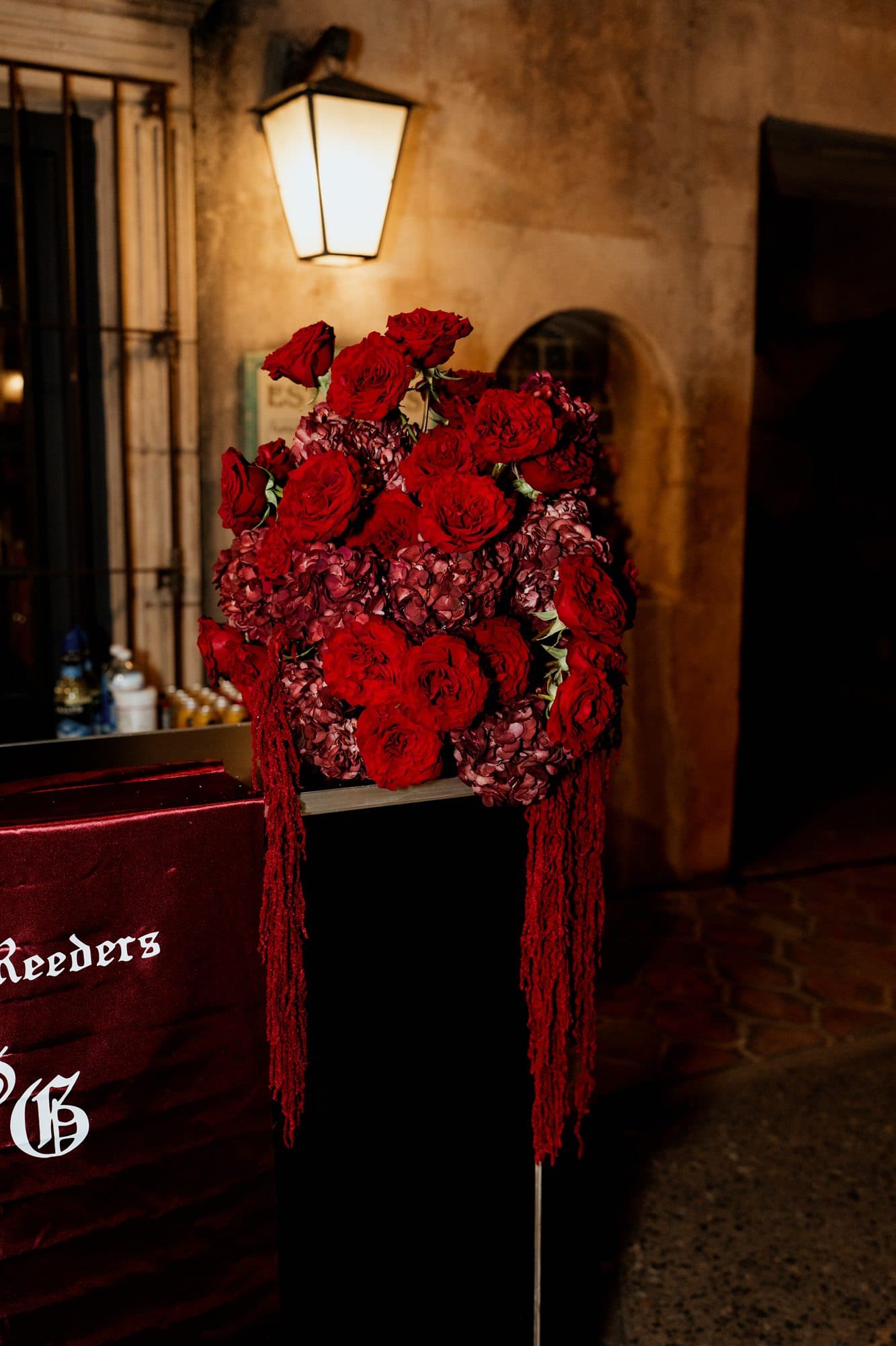 Red roses and cascading amaranthus above a burgundy velvet sign with gothic lettering
