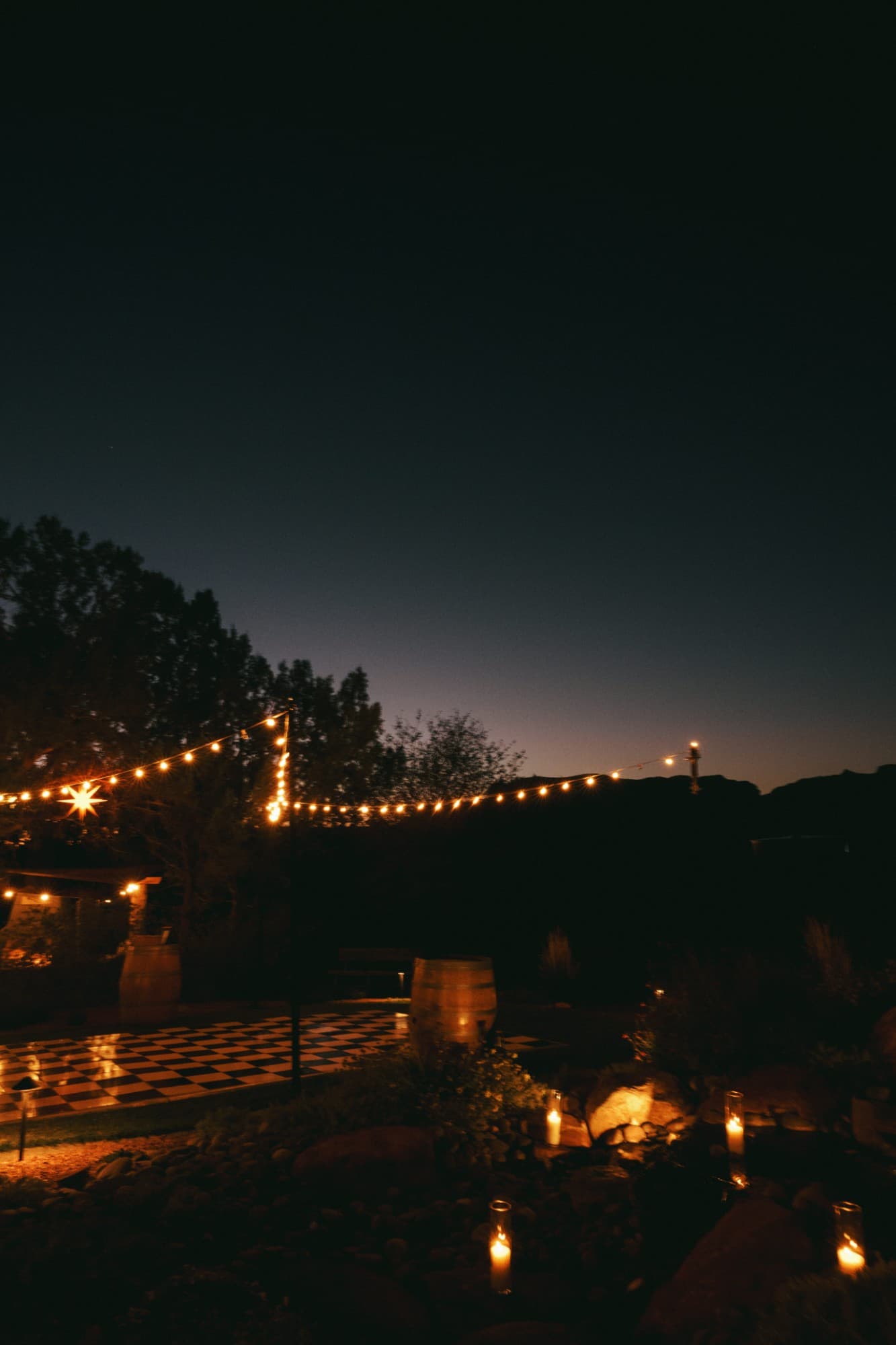 String lights over a checkered dance floor and candle-lined paths at dusk
