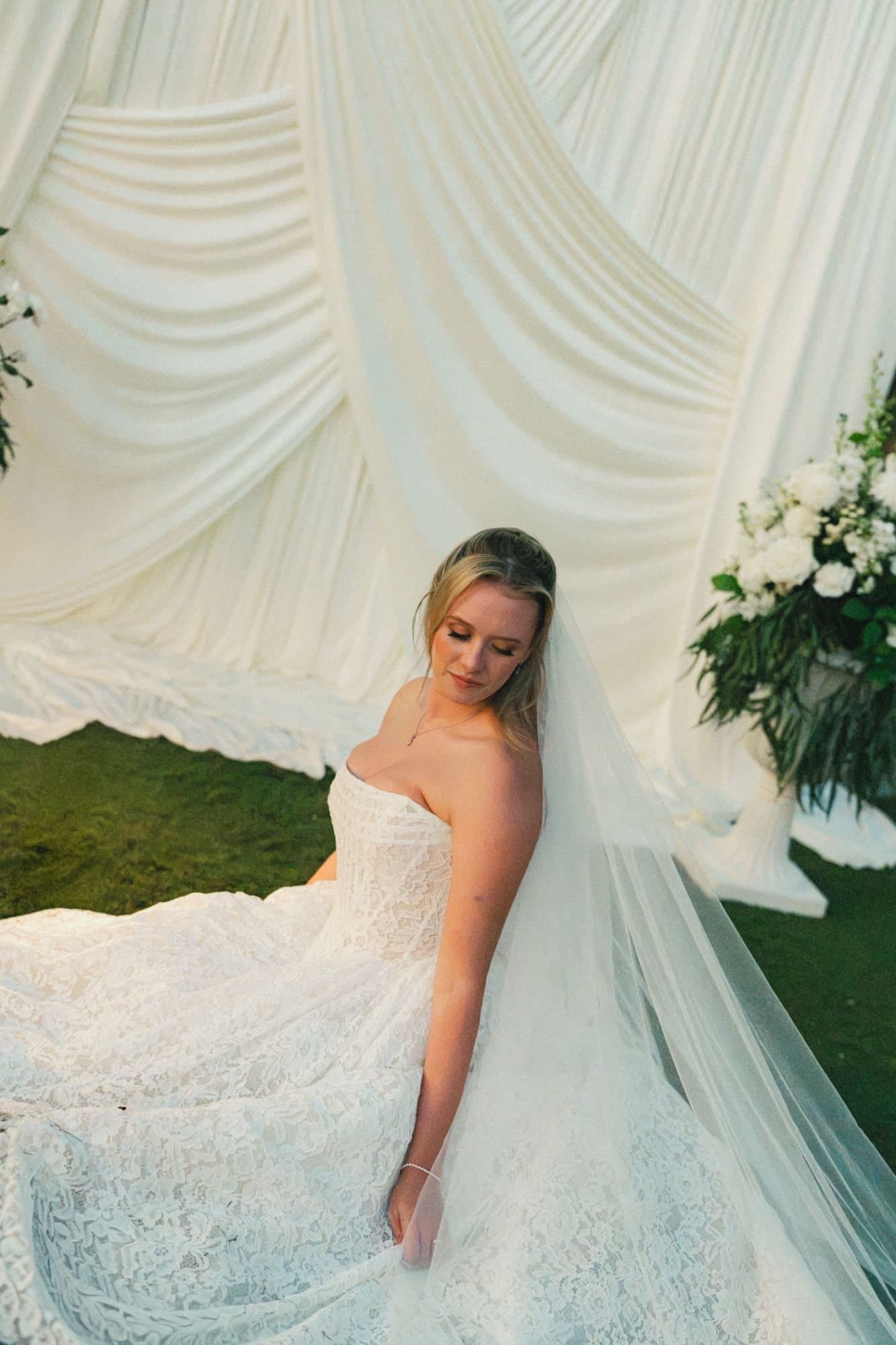 Sophia seated before dramatic ivory draping and urns of white florals
