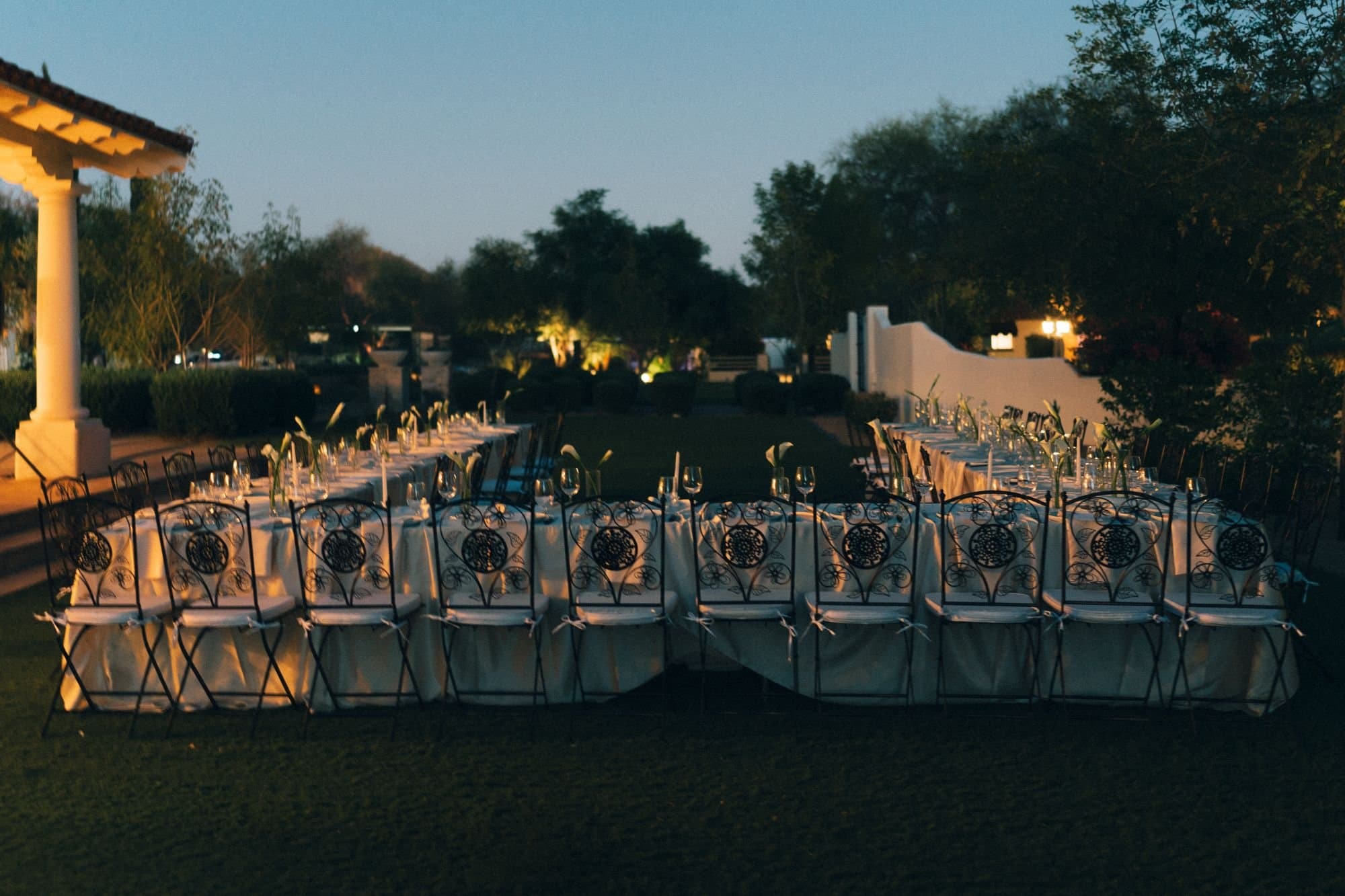 Long ivory dinner tables lined with wrought-iron chairs, calla lilies and taper candles at dusk