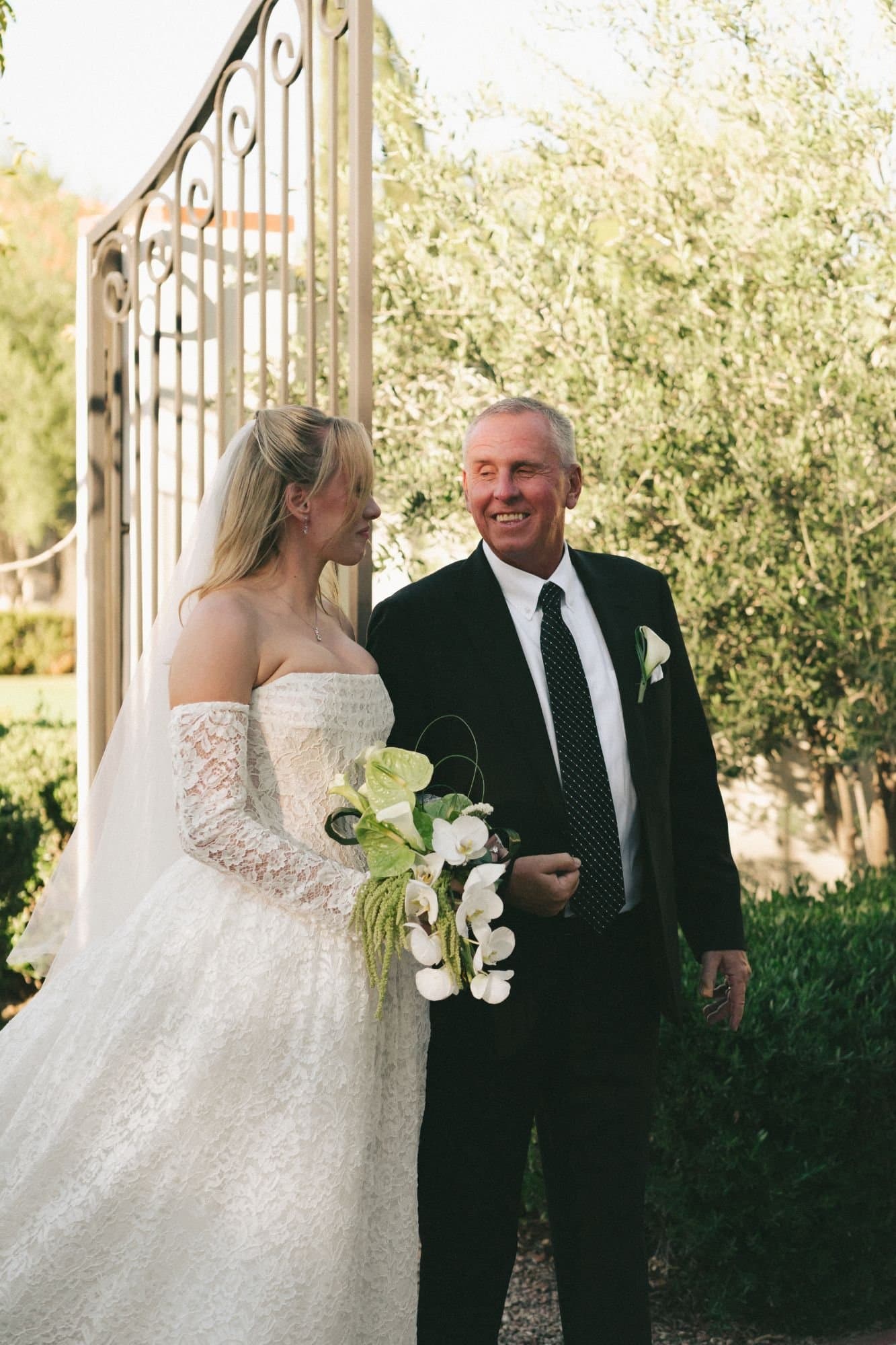Sophia and her father laughing beside the wrought-iron gate before the ceremony