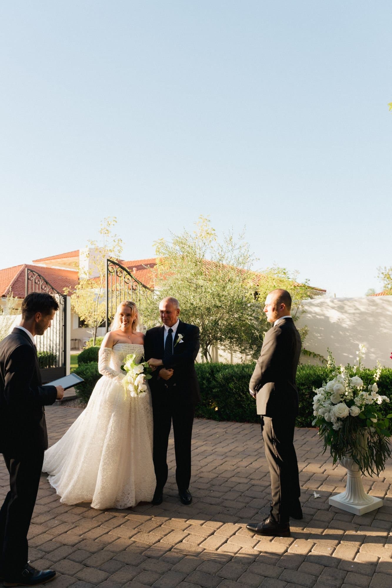 Sophia's father giving her away as Zachary waits by urns of white florals